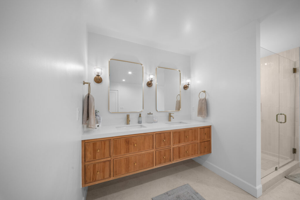 Floating double vanity with fluted wood cabinets, white quartz countertop, and brushed brass fixtures in a modern primary bathroom by RnD Builders Inc