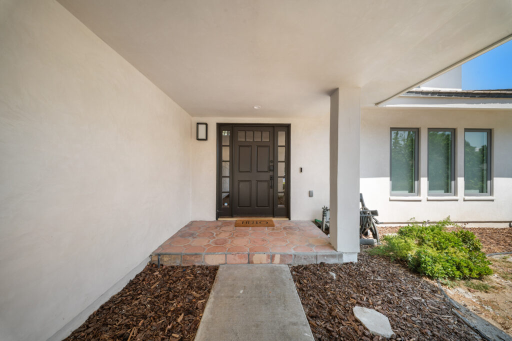 Covered front entryway with dark wood door, sidelights, and terracotta tile porch on white stucco home by RnD Builders Inc