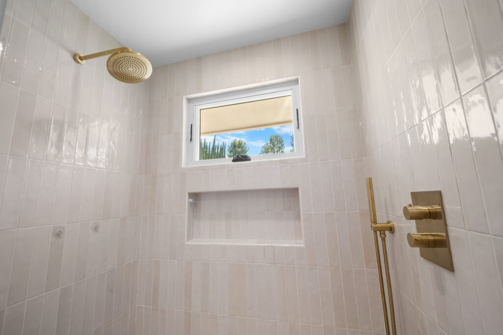 Walk-in shower with cream vertical subway tile, brass rain showerhead, and built-in niche by RnD Builders Inc
