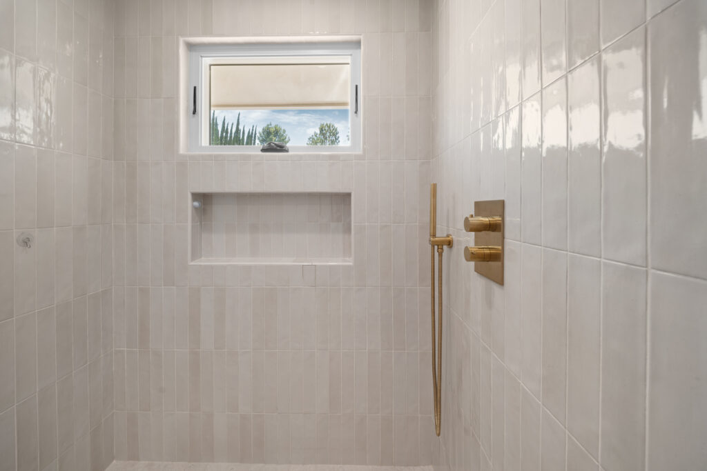 Walk-in shower with vertical white ceramic tile, recessed niche, and brushed gold fixtures by RnD Builders Inc