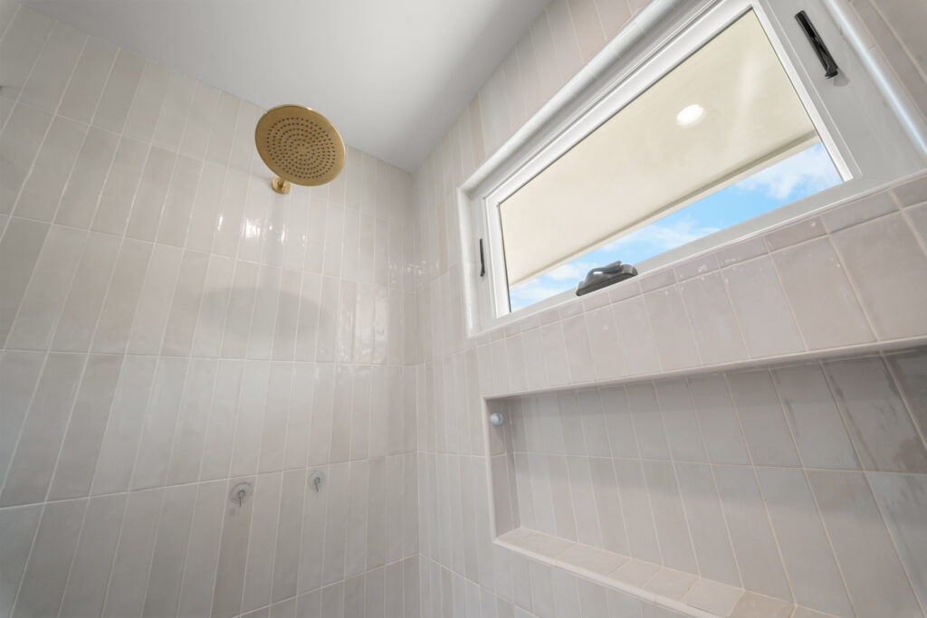 Walk-in shower with brushed gold rain showerhead, vertical cream tile, and built-in niche by RnD Builders Inc