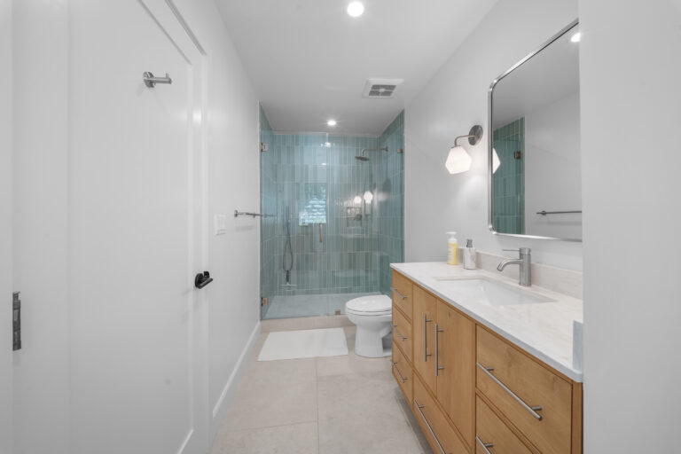 Modern full bathroom with teal vertical subway tile walk-in shower and natural wood vanity by RnD Builders Inc