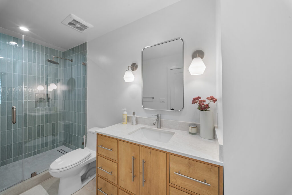 Modern bathroom with teal vertical subway tile shower, wood vanity, and quartz countertop by RnD Builders Inc