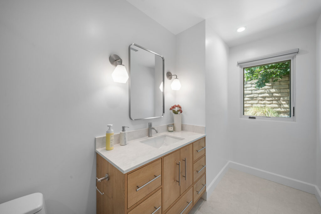 Modern bathroom vanity with light wood cabinets, quartz countertop, and brushed nickel fixtures by RnD Builders Inc