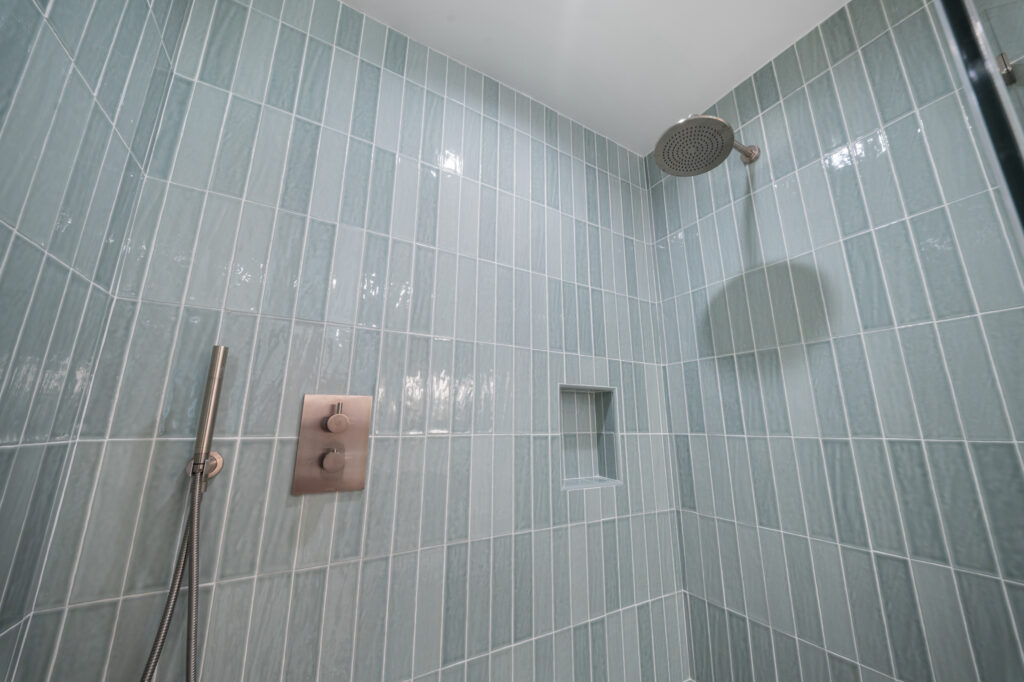 Walk-in shower with vertical seafoam green glass tile, brushed nickel rain showerhead and thermostatic valve by RnD Builders Inc