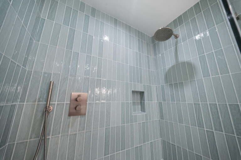 Walk-in shower with vertical seafoam green glass tile, brushed nickel rain showerhead and thermostatic valve by RnD Builders Inc