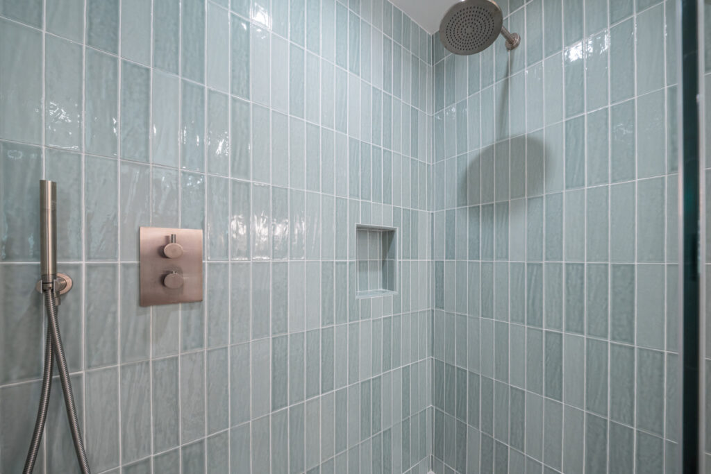Walk-in shower with vertical seafoam green glossy tile, rain showerhead, and brushed nickel thermostatic valve by RnD Builders Inc