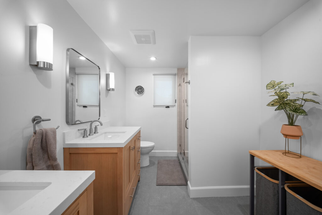 Modern full bathroom with warm wood vanity, white quartz countertop, and walk-in shower by RnD Builders Inc