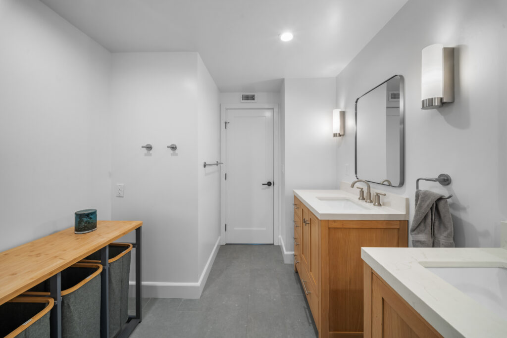 Modern bathroom with dual wood shaker vanities, white quartz countertops, and gray tile flooring by RnD Builders Inc