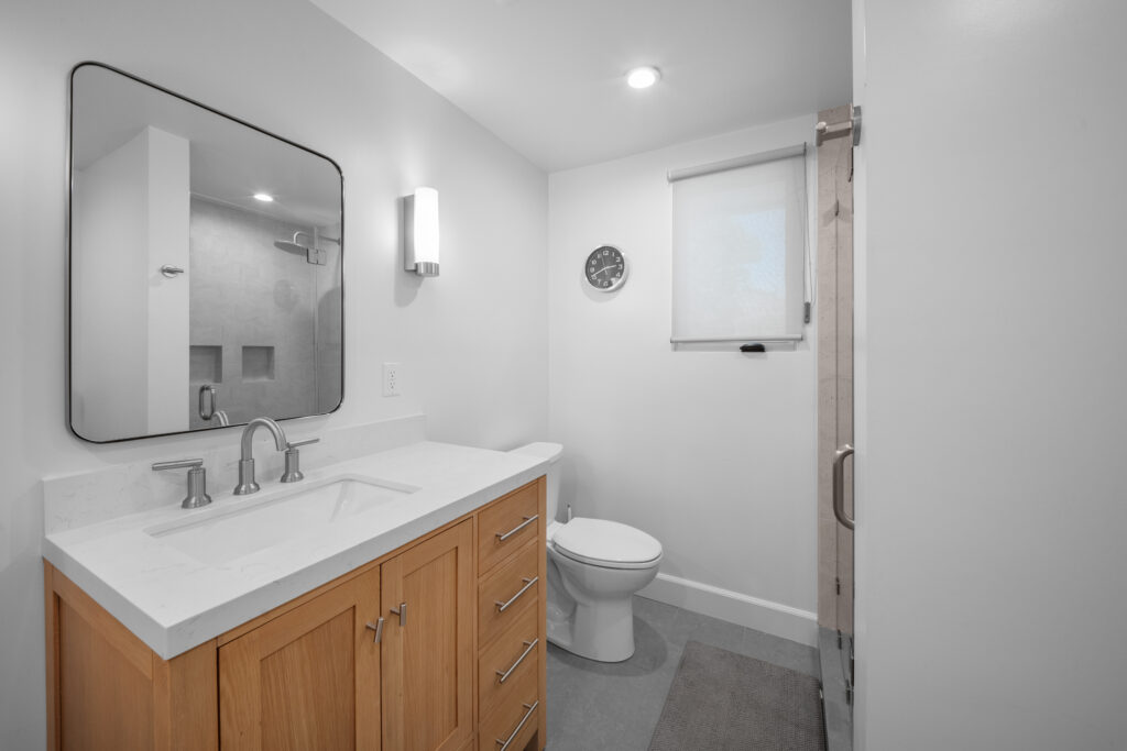 Modern full bathroom with warm wood vanity, white quartz countertop, and walk-in shower by RnD Builders Inc