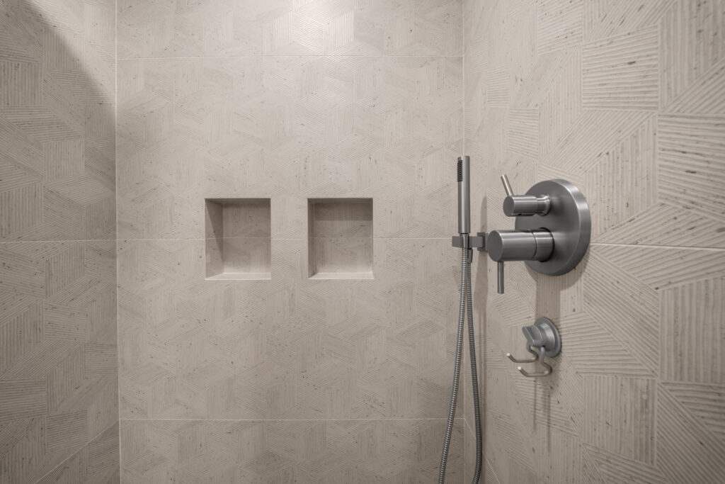 Walk-in shower with geometric textured tile, dual recessed niches, and brushed nickel fixtures by RnD Builders Inc