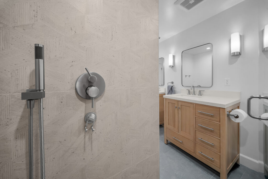 Modern bathroom with geometric textured tile shower and light wood shaker vanity by RnD Builders Inc