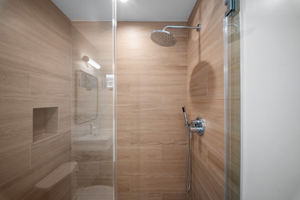 Walk-in shower with wood-look porcelain tile, rain showerhead, and frameless glass enclosure by RnD Builders Inc
