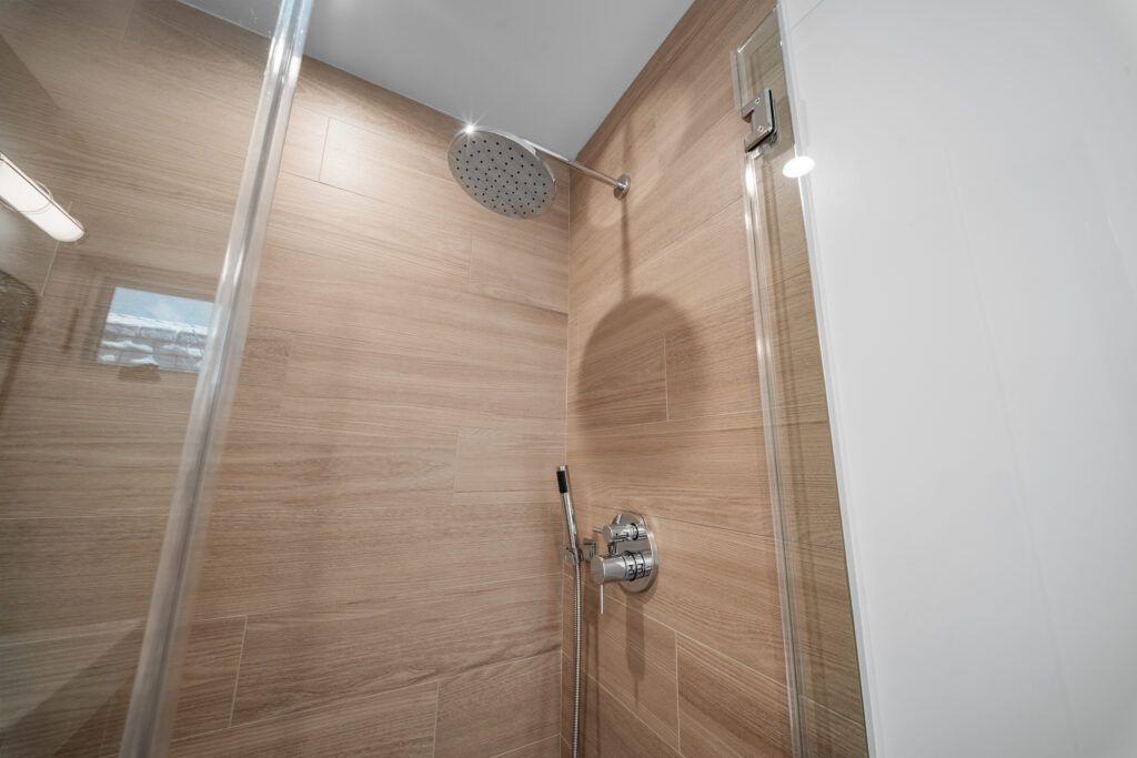 Walk-in shower with wood-look porcelain tile walls, round rain showerhead, and frameless glass door by RnD Builders Inc