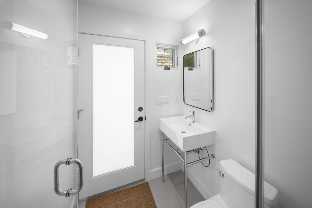 Modern white bathroom with console sink, glass shower door, and frosted glass entry door by RnD Builders Inc
