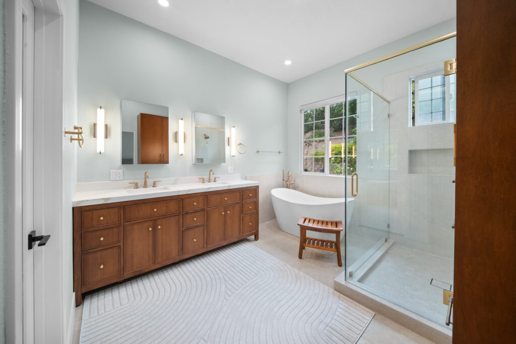 Master bathroom with fluted walnut double vanity, freestanding soaking tub, and frameless glass shower by RnD Builders Inc