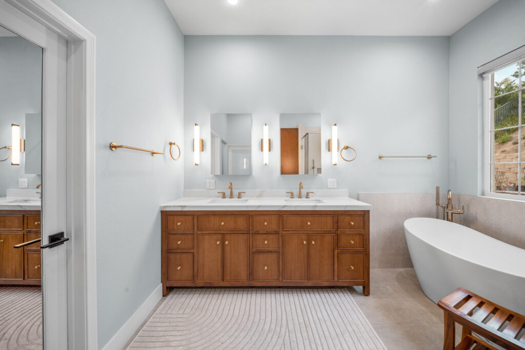 Master bathroom with fluted wood double vanity, white marble countertop, and freestanding soaking tub by RnD Builders Inc