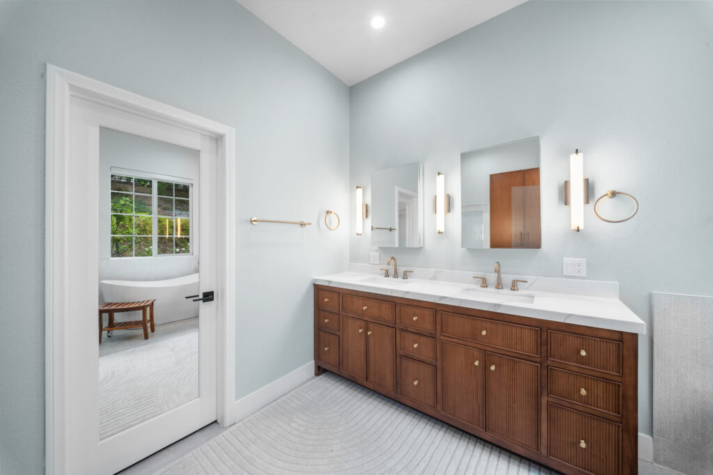 Primary bathroom with walnut fluted double vanity, white marble countertop, and freestanding soaking tub by RnD Builders Inc