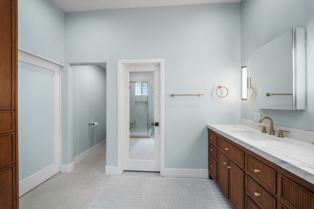 Primary bathroom with walnut fluted vanity, white marble countertop, and brushed gold fixtures by RnD Builders Inc