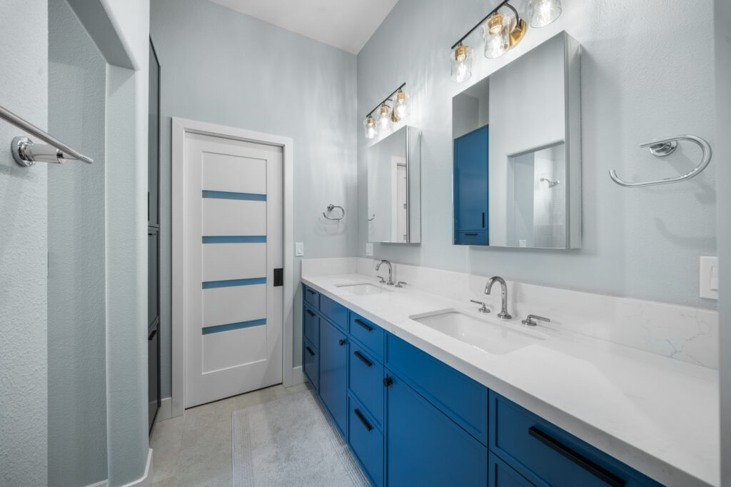 Double vanity bathroom with bold blue cabinets, white quartz countertop, and dual medicine cabinets by RnD Builders Inc