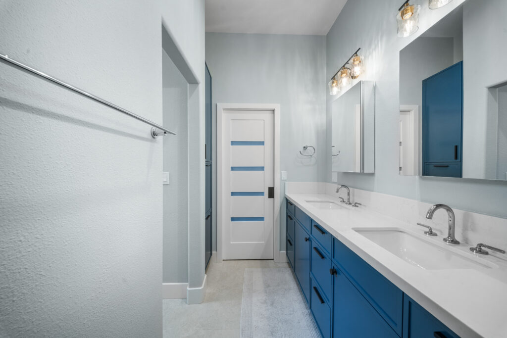 Dual-sink bathroom vanity with blue shaker cabinets, white quartz countertop, and modern glass pendant lighting by RnD Builders Inc