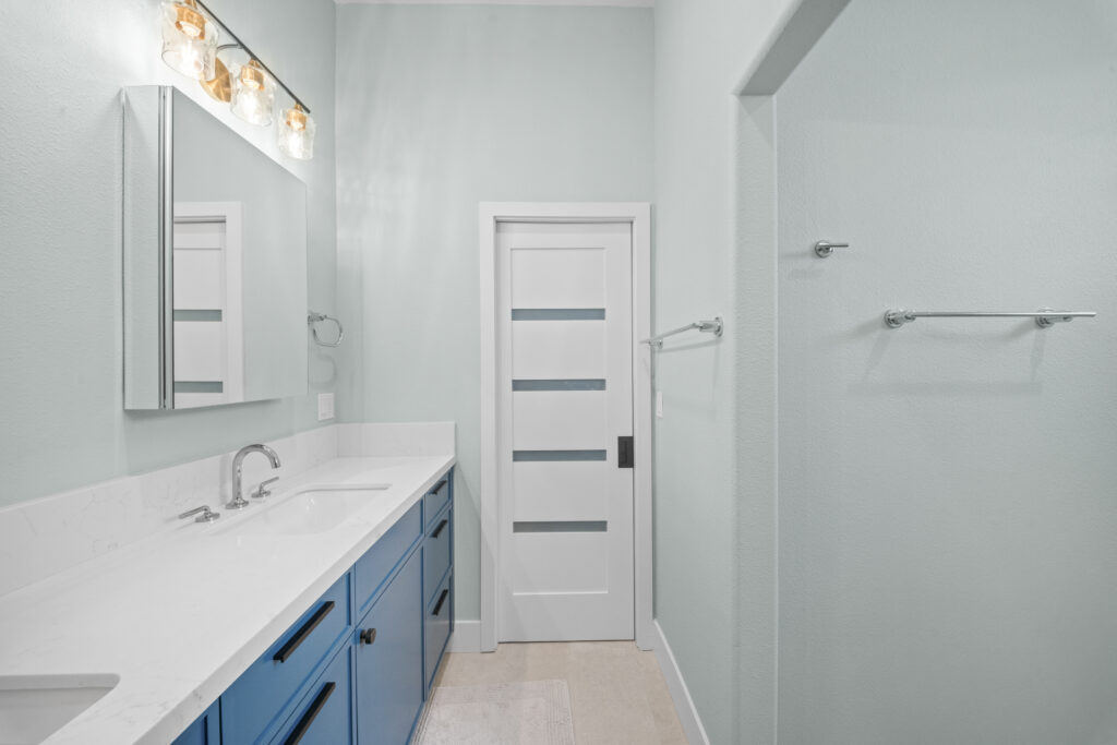 Modern bathroom with blue vanity, white quartz countertop, and glass-panel interior door by RnD Builders Inc