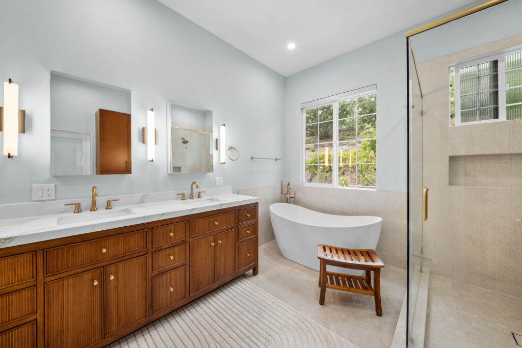Luxury primary bathroom with fluted wood double vanity, freestanding soaking tub, and glass shower enclosure by RnD Builders Inc
