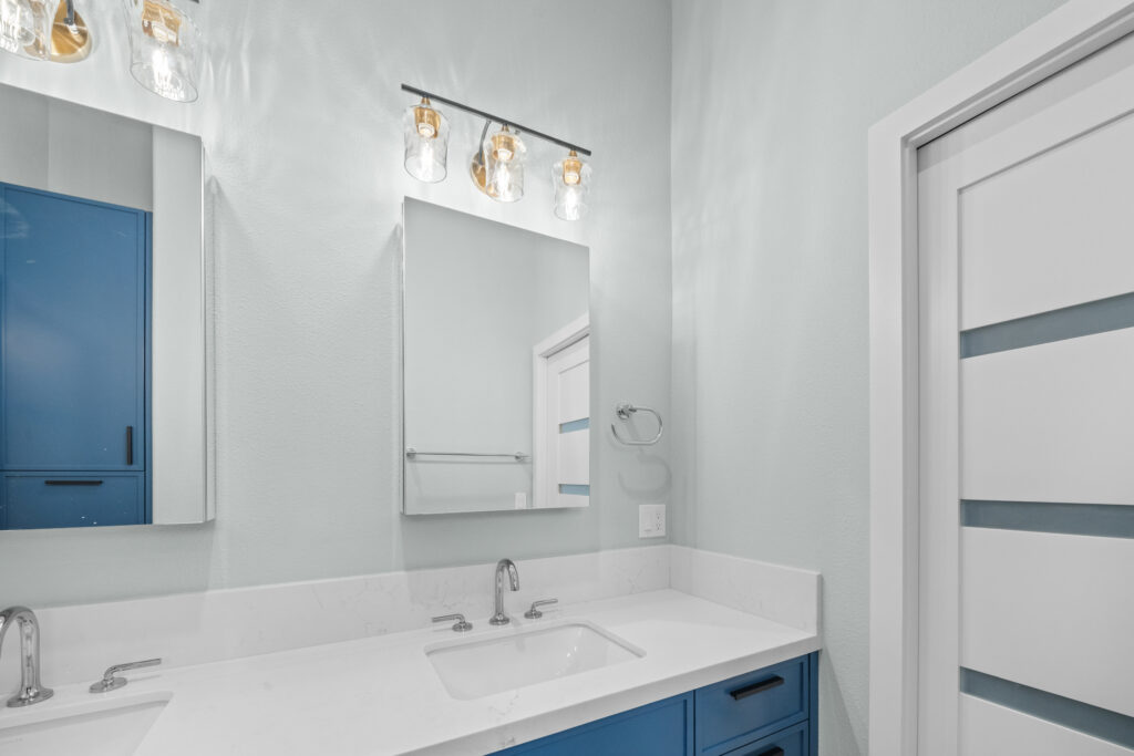 Bathroom vanity with blue shaker cabinets, white quartz countertop, and gold pendant light bar by RnD Builders Inc