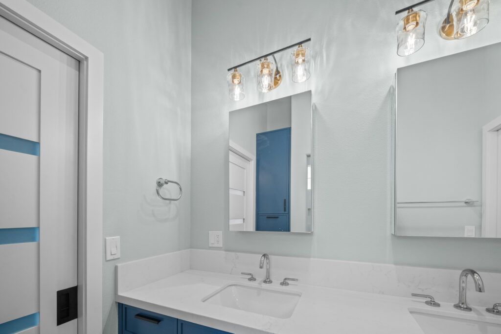 Double-sink bathroom vanity with blue cabinets, white quartz countertop, and glass pendant vanity lights by RnD Builders Inc