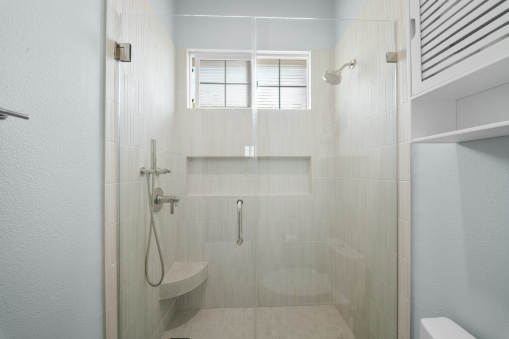 Walk-in shower with vertical white tile, frameless glass door, and built-in bench by RnD Builders Inc