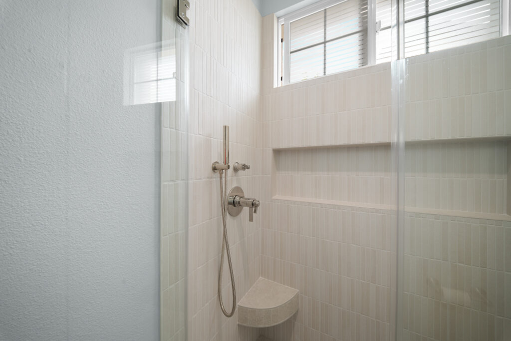 Walk-in shower with white vertical subway tile, built-in niche, and brushed nickel handheld fixture by RnD Builders Inc