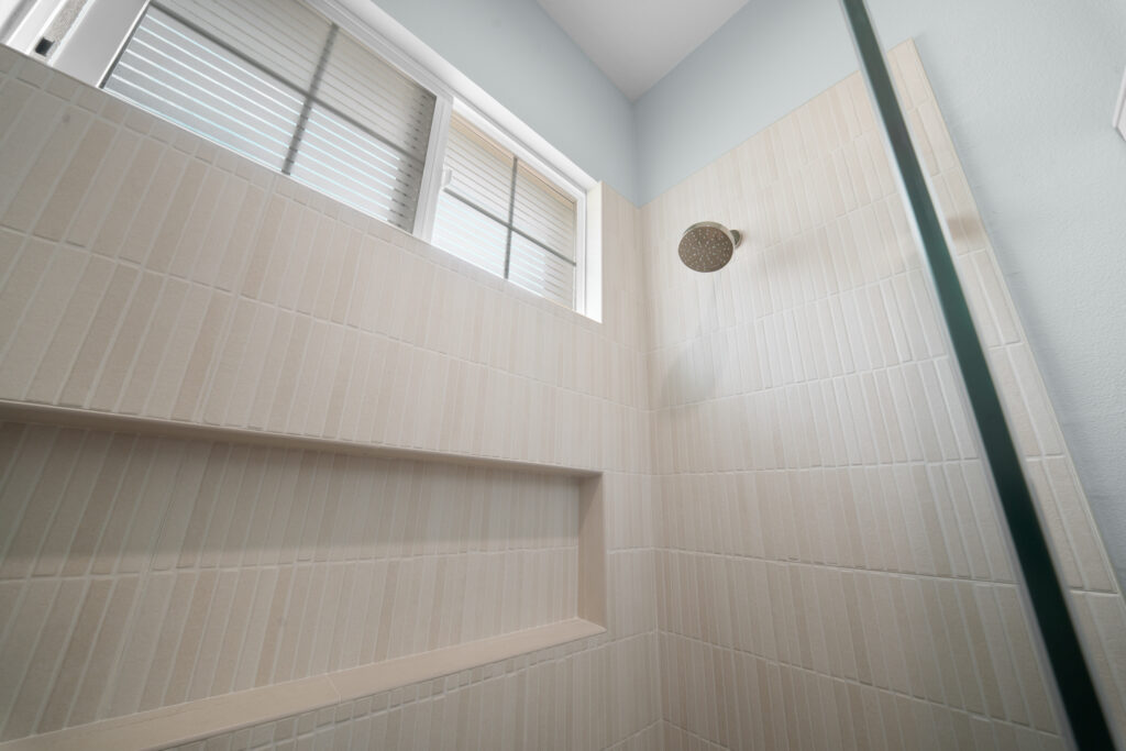Tiled walk-in shower with recessed niche, rain showerhead, and natural light window by RnD Builders Inc