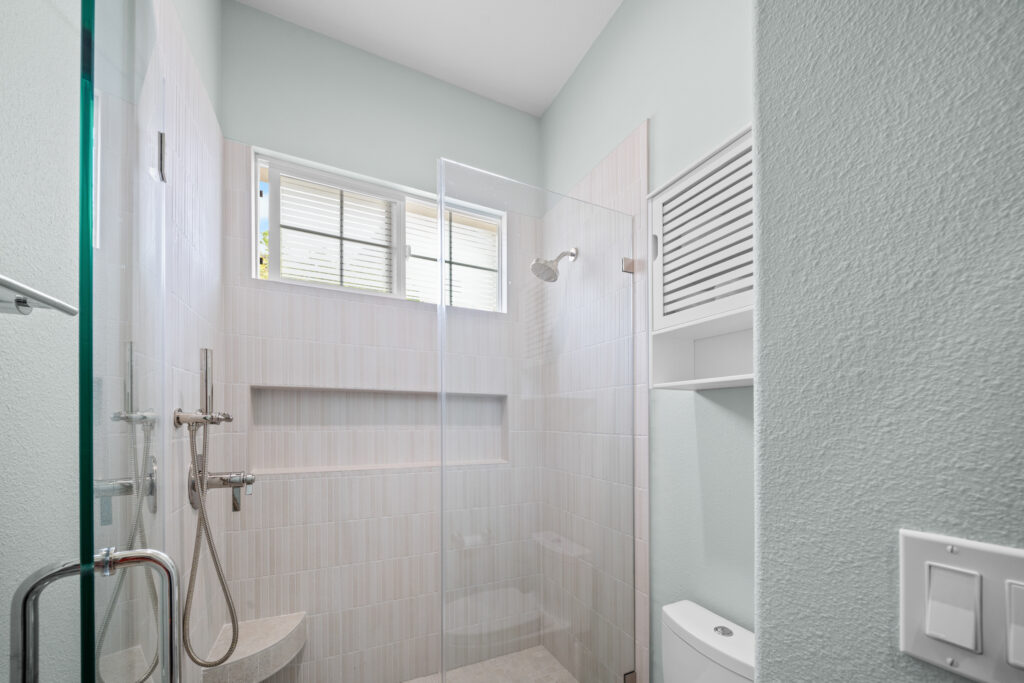 Walk-in glass shower with vertical subway tile, built-in niche, and chrome fixtures by RnD Builders Inc