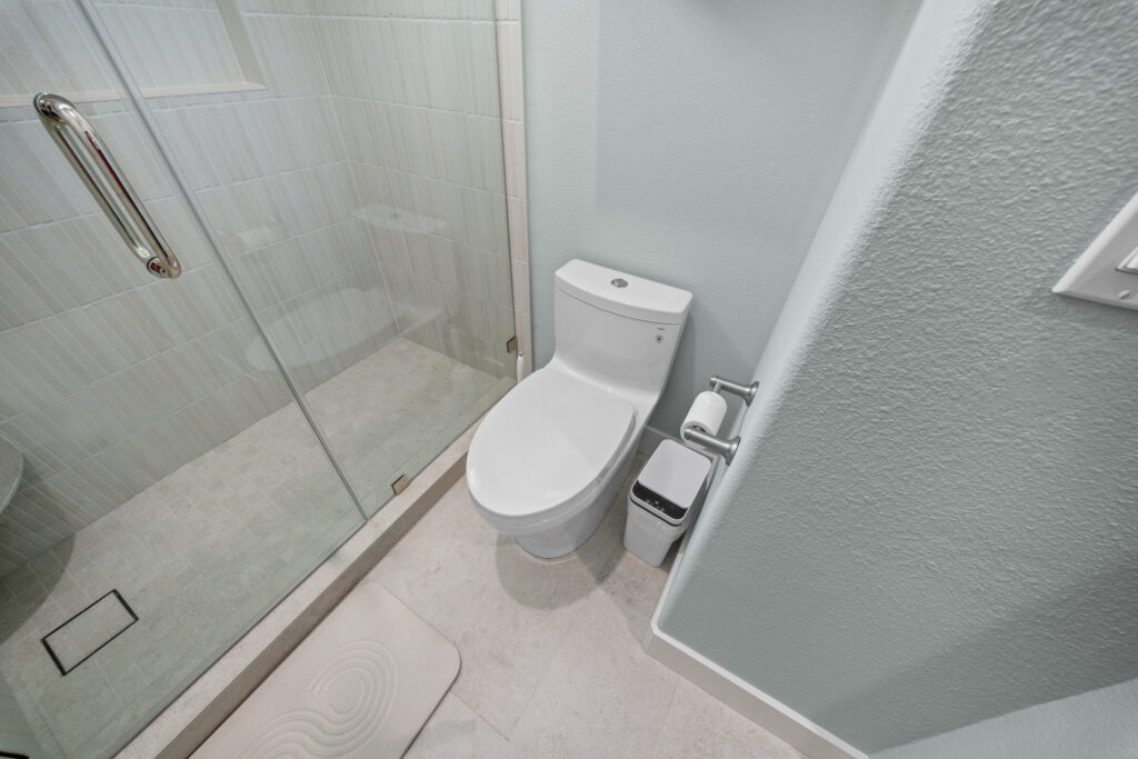 Modern bathroom with frameless glass shower, elongated toilet, and light grey subway tile by RnD Builders Inc