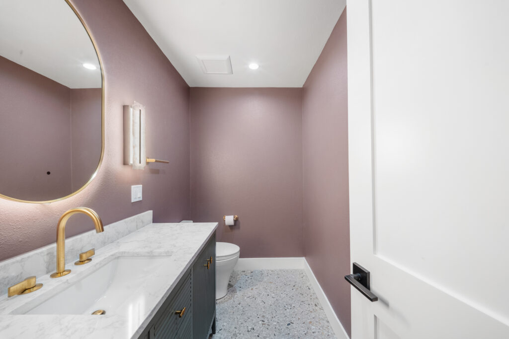 Powder room with mauve walls, terrazzo floor, marble vanity, and brushed gold fixtures by RnD Builders Inc