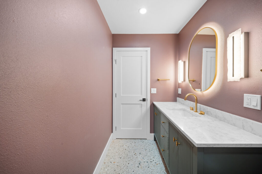 Bathroom with green fluted vanity, white marble countertop, gold fixtures, and oval backlit mirror by RnD Builders Inc