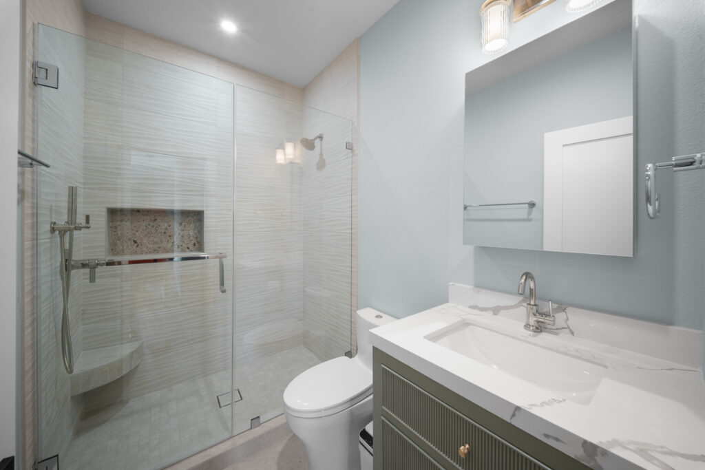 Modern bathroom with frameless glass shower, quartz vanity, and fluted sage green cabinet by RnD Builders Inc