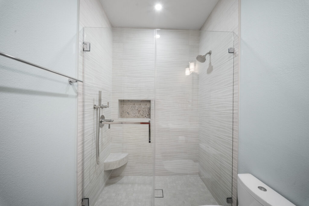 Walk-in shower with white wave-textured tile, frameless glass enclosure, and built-in niche by RnD Builders Inc