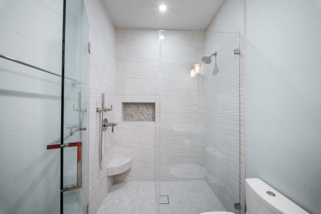 Modern walk-in shower with textured wave tile, frameless glass enclosure, and built-in niche by RnD Builders Inc
