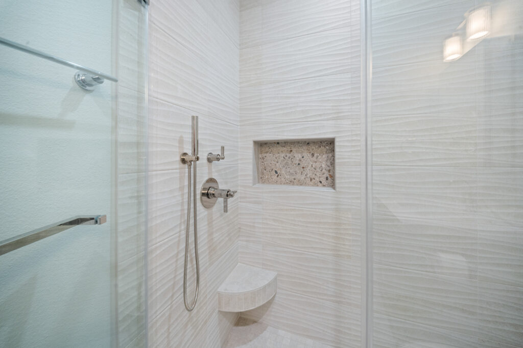 Walk-in shower with textured wave wall tile, mosaic niche, and chrome handheld fixture by RnD Builders Inc