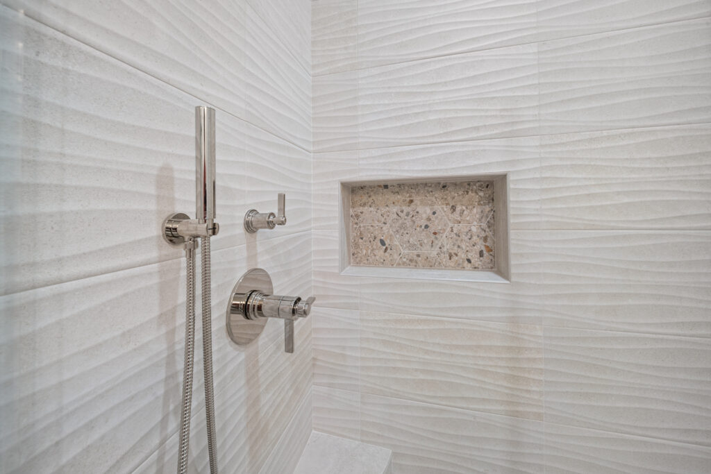 Walk-in shower with 3D wave wall tile, polished nickel hand shower, and hexagon mosaic niche by RnD Builders Inc