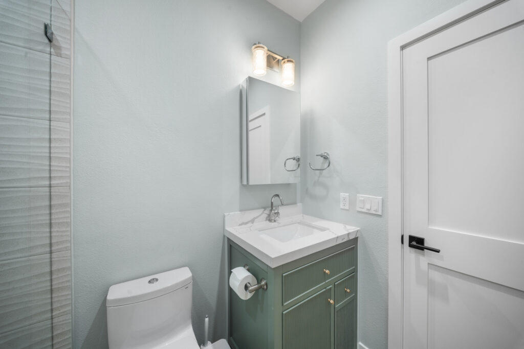 Small full bathroom with sage green fluted vanity, white quartz countertop, and glass shower enclosure by RnD Builders Inc