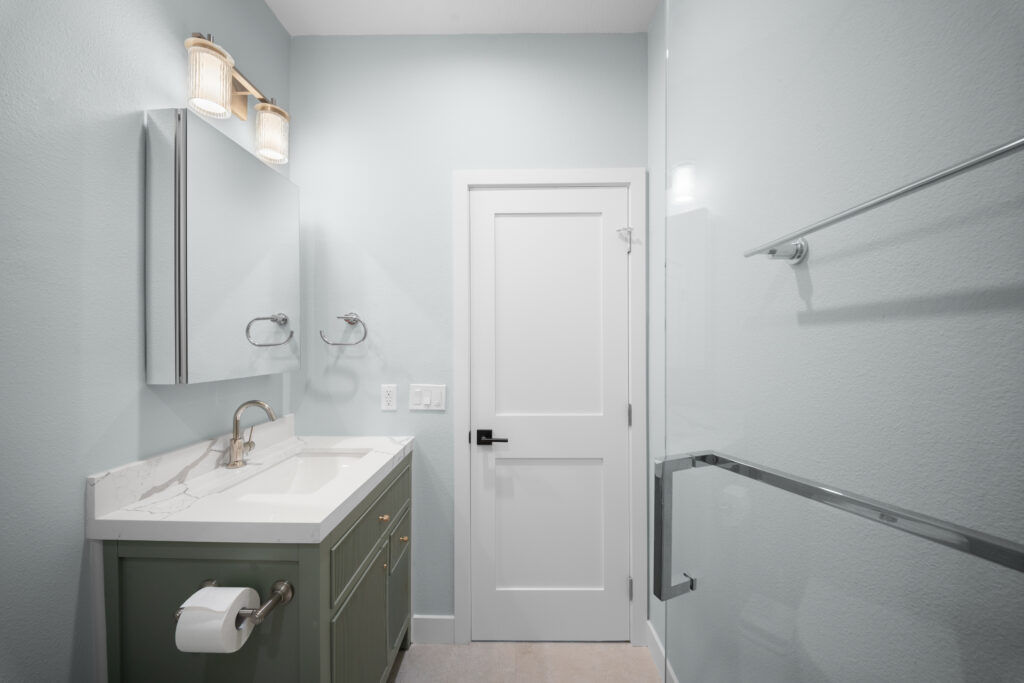 Light blue bathroom with sage green fluted vanity, quartz countertop, and glass shower enclosure by RnD Builders Inc