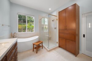 RnD_ThousandOaks_2926_5 Master bathroom with freestanding soaking tub, glass walk-in shower, and tall walnut linen cabinet by RnD Builders Inc