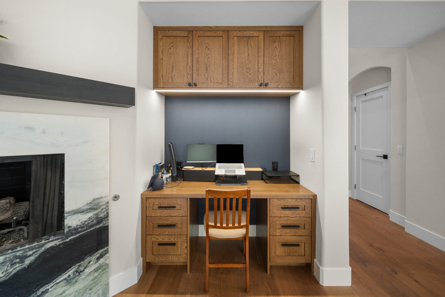Built-in oak home office nook with upper shaker cabinets, under-cabinet lighting, and pedestal desk by RnD Builders Inc