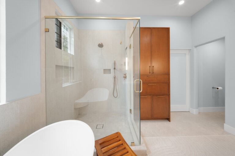 Luxury master bathroom with glass shower enclosure, freestanding tub, and warm wood cabinetry by RnD Builders Inc