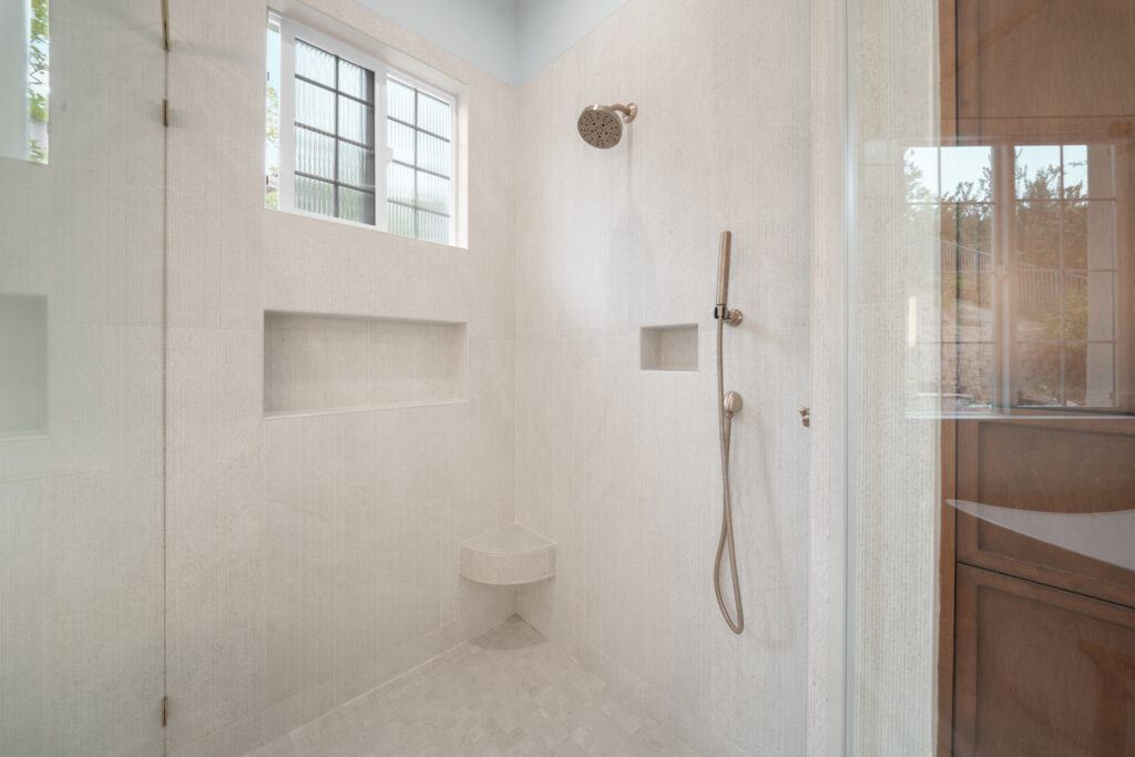 Walk-in shower with large-format white tile, dual niches, corner bench, and brushed nickel fixtures by RnD Builders Inc