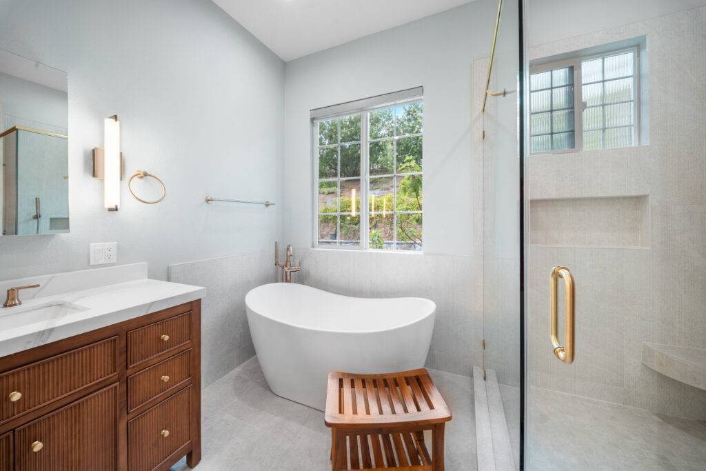 Luxury primary bathroom with freestanding soaking tub, fluted walnut vanity, and glass-enclosed shower by RnD Builders Inc