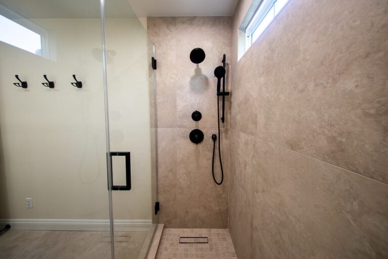 Walk-in shower with large-format beige tile, matte black fixtures, and frameless glass door by RnD Builders Inc