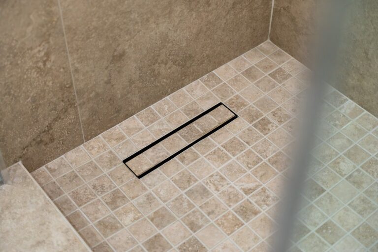 Beige travertine mosaic tile shower floor with matte black linear drain by RnD Builders Inc